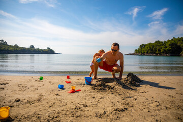 Father and daughter building sand castle on the beach at sunny day. 