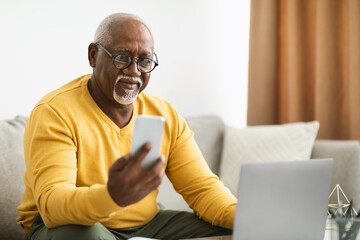 Mature African American Businessman Using Cellphone And Laptop Working Indoors