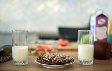 Two glasses with white milk with cookies and sesame seeds on wooden table in kitchen, home breakfast and healthy food background