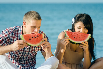 guy and a girl on the seashore eating a ripe watermelon