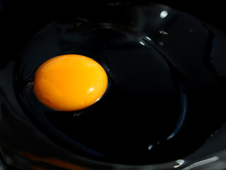 A raw egg broken without a shell is spilled on a black plate
