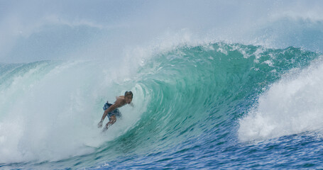 Young man surfer surfing tropical ocean wave riding barrel tube