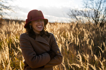 Naklejka na ściany i meble Young smiling female in autumn field dressed with coat and hat. Colorful sunset in the field with young model.