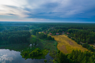 Idyllic aerial landscape of the green forest, small lake and fields. Blue sky with clouds. 