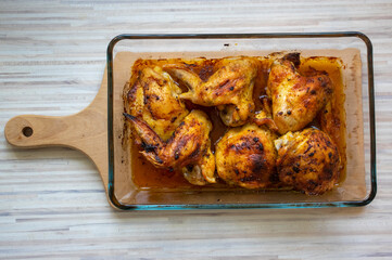 Roasted chicken wings and thighs in glass transparent baking dish on wooden table, ready to eat