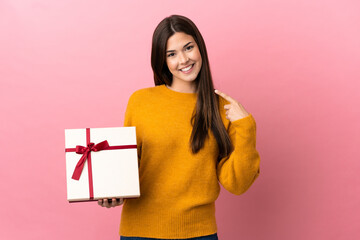 Teenager Brazilian girl holding a gift over isolated pink background giving a thumbs up gesture