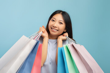 Black friday concept. Happy asian lady after successful shopping carrying bright paper bags, blue background