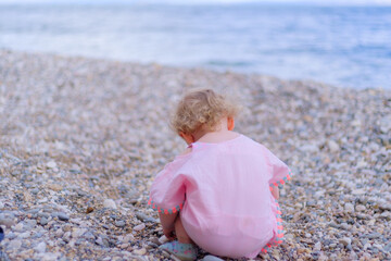 Blonde little girl crouch and looking for a beautiful stone or rock at beach, holiday concept idea