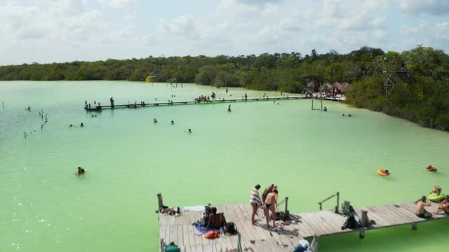 Fly over wooden piers at lake shore with people enjoying hot sunny day. Natural swimming pool with shallow water in tropical destination. Kaan Luum lagoon, Tulum, Yucatan, Mexico