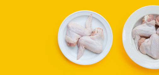 Fresh raw chicken wings in white dishes on yellow background.