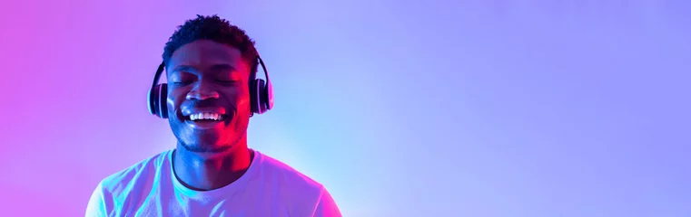 Foto op Aluminium Handsome young black man wearing headphones, listening to music with closed eyes in neon light, banner design © Prostock-studio