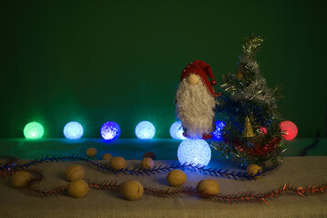 Santa Claus toy near the Christmas tree around the bright colored balls. Christmas decoration on the table with many nuts