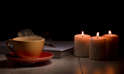 Obraz na płótnie Canvas Cup of hot coffee with green smoke, books and burning candles. Desk table in power supply cut