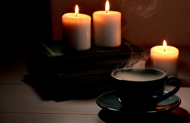 Cup of hot coffee with green  smoke, books and burning candles. Desk table in power supply cut