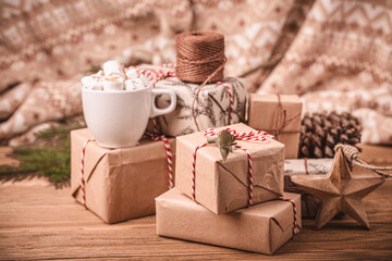 Fototapeta na wymiar Pile of Christmas wrapped presents with twine string roll, fir tree branch, marshmallow cacao cup, Christmas toy star at wooden background. Xmas decoration, cozy festive composition, space for text