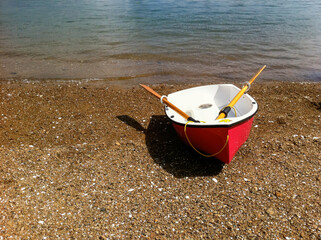 Red dinghy, with yellow oars on a deserted pebble beach, summer, Mansion House Bay, Kawau Island, New Zealand