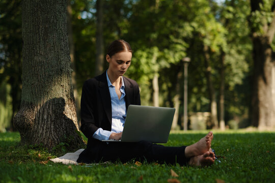 Side view of woman sitting in a park on green grass with a lapot and notebook, outdoor worker, remote work.