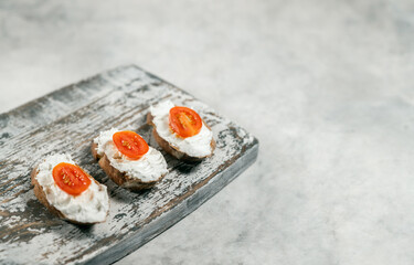 Three cream cheese sandwiches with tomatoes on the wooden board on grey background, free space for text