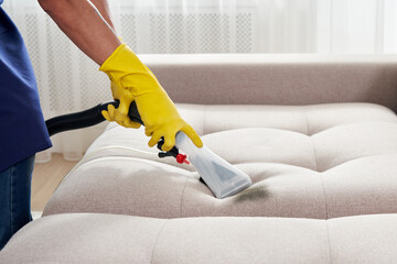 Close-up of housekeeper holding modern washing vacuum cleaner and cleaning dirty sofa with stain with professionally detergent. Professional springclean at home concept