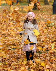 Girl playing with fallen yellow leaves. Portrait of a happy child in an autumn park.