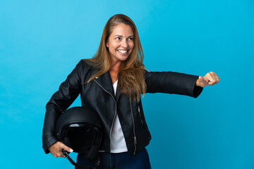 Middle age woman holding a motorcycle helmet isolated on blue background giving a thumbs up gesture