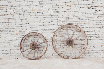 Fototapeta na wymiar Two vintage wooden wheels. Antique masonry in beige shades. Beautiful textured background from natural stone. Hand laid sandstone or shell rock wall. Symbol of energy, life cycle, movement.