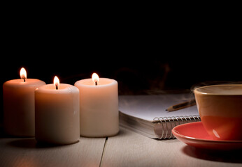 three lit candles, with notebook, pencil, and partial view of a cup of hot soup, electric blackout.