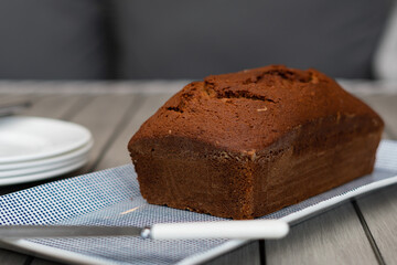 Straight on view of home baked banana bread served on a blue and white rectangle dish with plates and knife in view. Home setting with copy space available