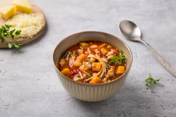 Vegan seasonal italian minestrone soup with pumpkin, beans, tomatoes, bell peppers, pasta and herbs on gray textured background