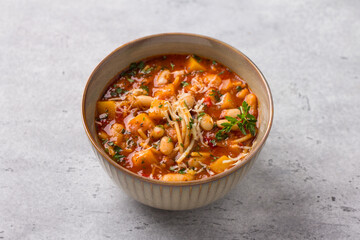 Vegan seasonal italian minestrone soup with pumpkin, beans, tomatoes, bell peppers, pasta and herbs on gray textured background