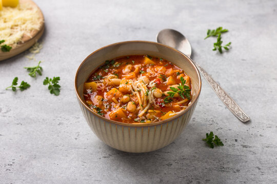 Vegan seasonal italian minestrone soup with pumpkin, beans, tomatoes, bell peppers, pasta and herbs on gray textured background