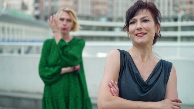 Portrait of confident woman looking away winking smiling as jealous bad friend with crossed hands standing at background. Concept of rivalry and jealousy. Slow motion