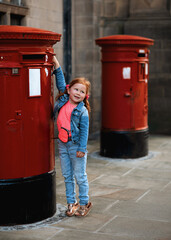 a red-haired girl in a denim jacket and a pink T-shirt throwing a letter into a red mailbox