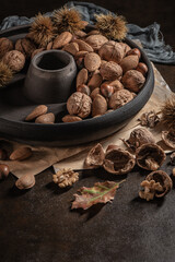 Obraz na płótnie Canvas Modern design black ceramic bowl with walnuts, hazelnuts, almonds, chestnut hedgehogs on dark countertop and background. Autumn table