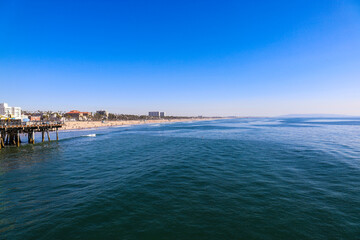 Fototapeta na wymiar a stunning shot of vast blue ocean water and the cityscape along the beach with brown sand, hotels and buildings and blue sky at Santa Monica Pier in Santa Monica California USA
