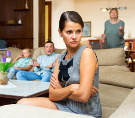 Upset young woman sitting at sofa during quarrelling between family on background at home