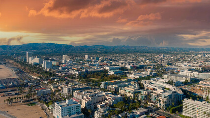 an aerial shot of the cityscape of the City of Santa Monica with vast miles of buildings and palm trees with majestic mountain ranges and powerful clouds at sunset in Santa Monica California USA - obrazy, fototapety, plakaty