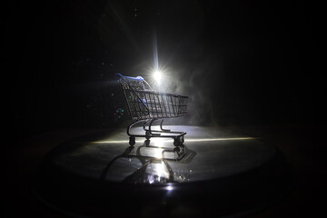 Empty shopping trolley on dark toned foggy background with some copy space. Financial crisis...