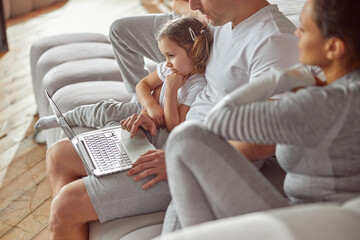 Top view of relaxed parents with son and daughter sitting on sofa and watching video on notebook