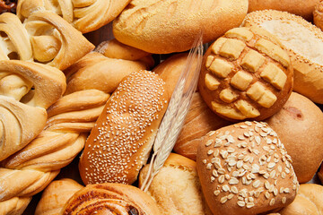 Close up of different types of breads and golden buns with ears of wheat. Food and bakery concept. Salty and sweet food. Bakery and carbohydrates.