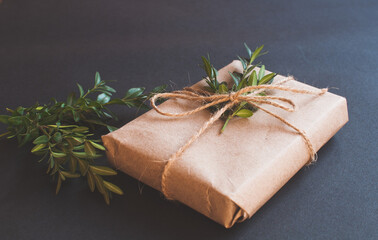 Craft gift box with knot natural with green leaves on black background