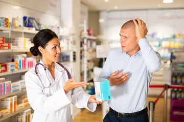 Oriental woman pharmacist consulting man about headache in drugstore and proposing medicine to him.