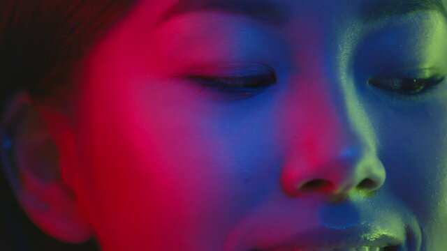 Close up portrait of young pretty asian woman posing to camera in bright colorful neon lights and smiling