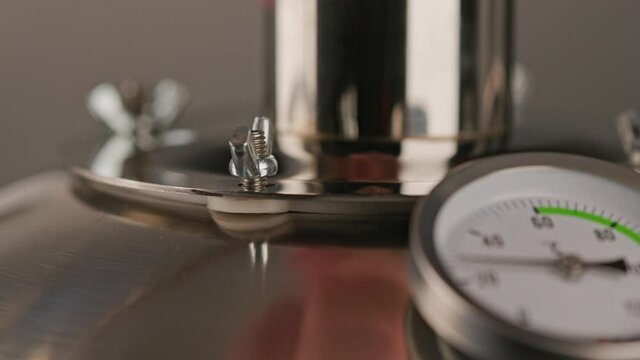 bare caucasian hand unscrewing and screwing out zink coated wing nut on domestic stainless steel alcohol mashine