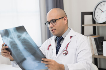 Young asian doctor working from home looking x-ray film. The patient's symptoms from the X-ray and the results are reported online via video conferencing.