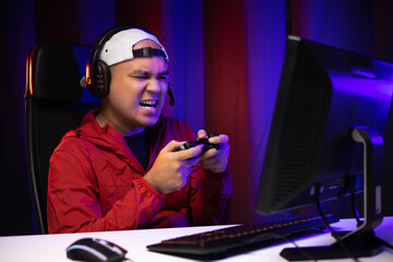 Angry asian gamer man playing computer pc. He lose in the game. Missed the chance to become a champion in tournament. Unhappy upset Indian streaming video game online and lost. © Chanakon