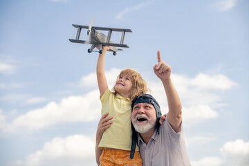 Young grandson and old grandfather playing with toy plane against summer sky background.