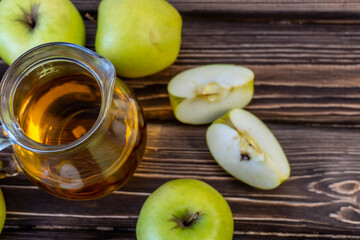 Green apples and jug with apple juice on wooden background