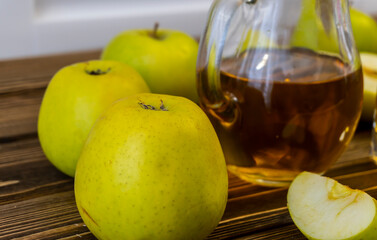 Green apples and jug with glass with apple juice on wooden background