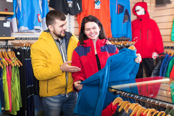 Young couple choosing track jacket in sports clothes shop